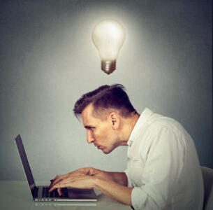 Person mit einer Glühbirne über dem Kopf arbeitet gebückt am Computer.