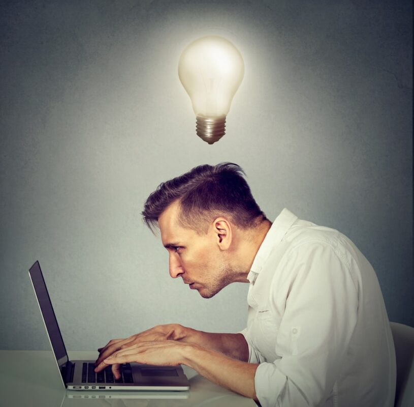 Person mit einer Glühbirne über dem Kopf arbeitet gebückt am Computer.