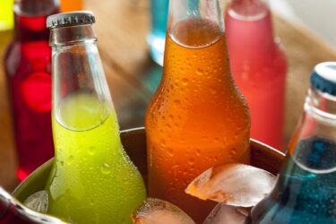 Image de bouteilles de boissons sucrées réfrigérées contenant un liquide coloré.