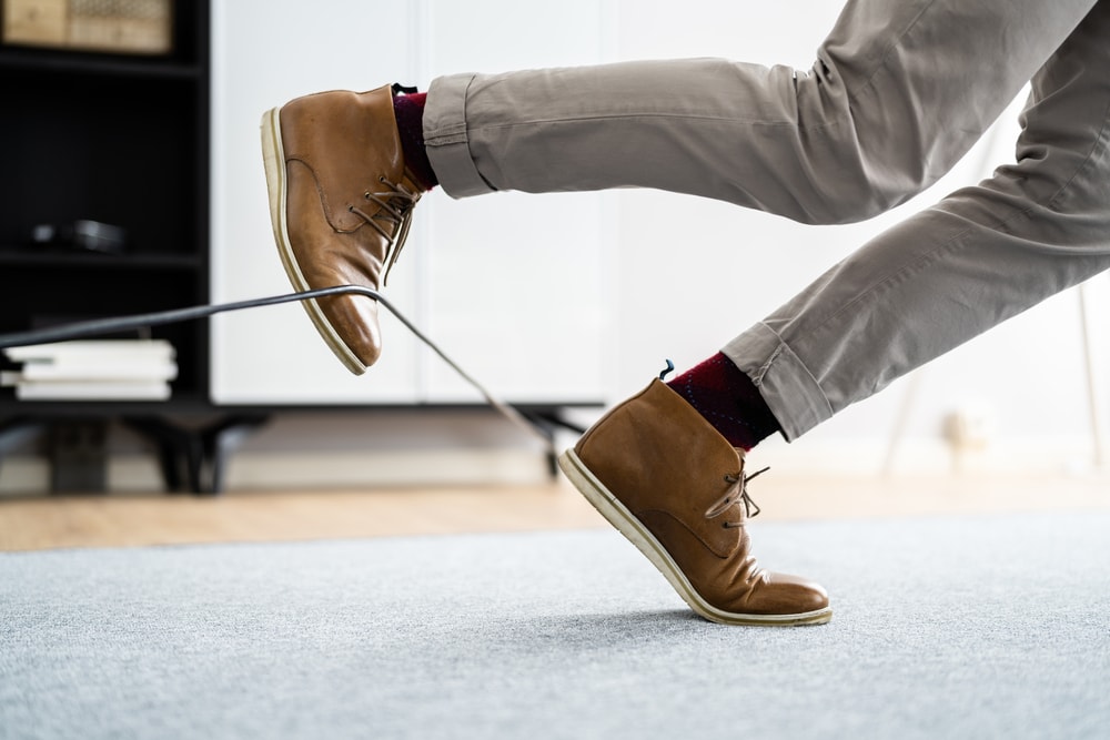 Une personne portant des chaussures brunes trébuche sur un câble. Probablement dans un environnement de bureau.